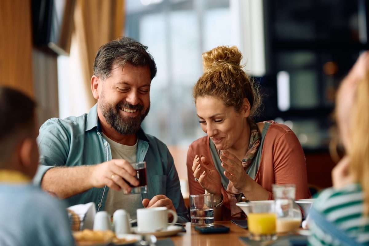 BeachesUSA-PeopleEating-Shutterstock | Beaches USA Rentals & Management, LLC A smiling group of adults sharing a meal at a restaurant, raising glasses in a toast.